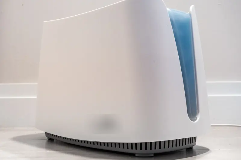 White portable humidifier with a blue water tank standing on the floor against a plain white wall